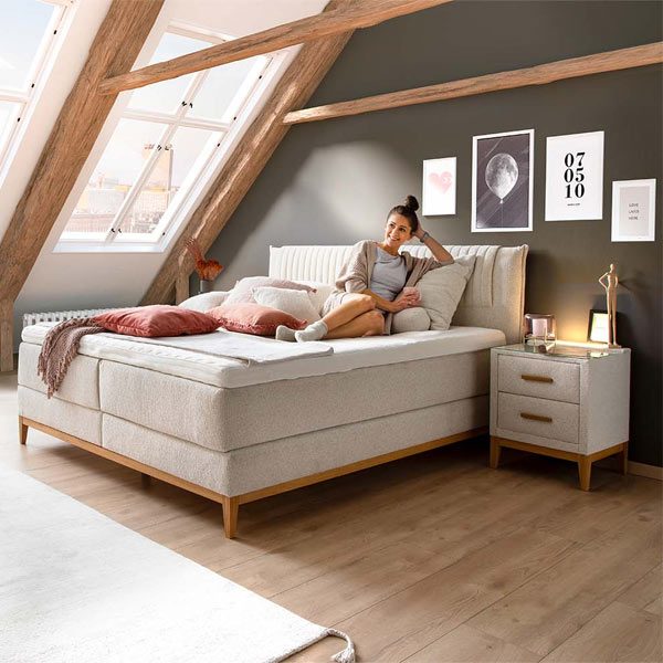 Boxspringbett mit hellem Stoffbezug unter einer Dachschräge