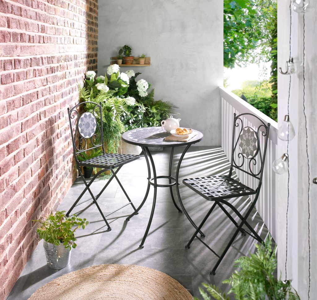 Balkon mit Bistrotisch, zwei Stühlen und Blumen vor einer Backsteinwand