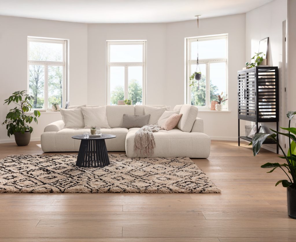 Helles Wohnzimmer mit weißem Ecksofa, Rundteppich und Erkerfenstern