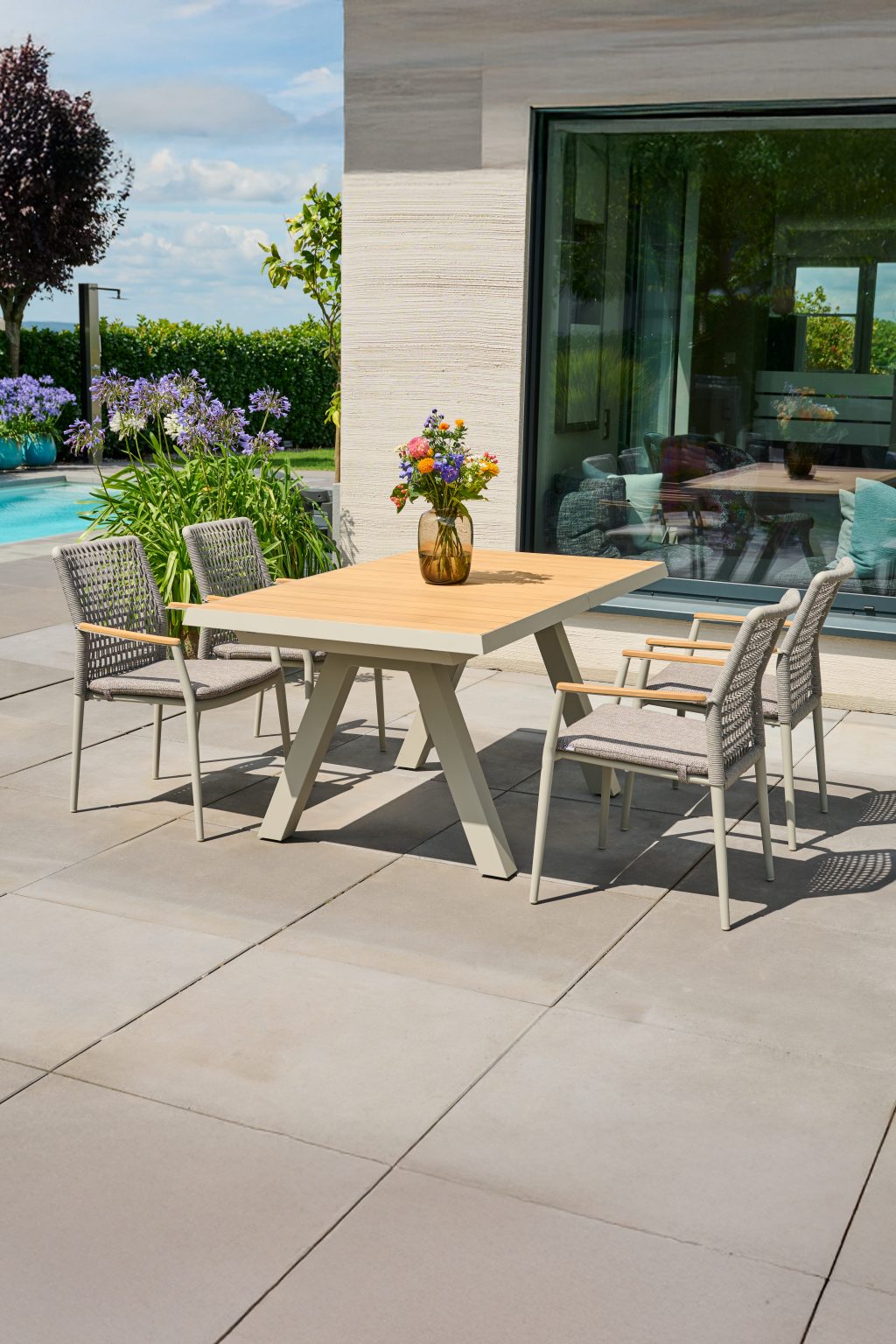 Gartentisch aus Holz mit vier Stühlen auf einer Terrasse vor dem Pool