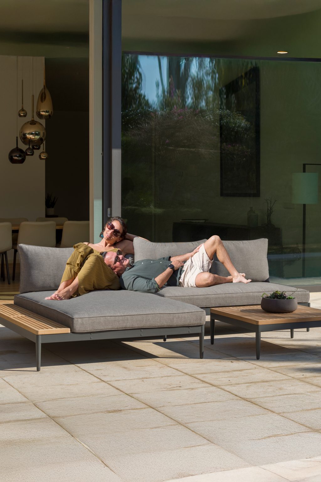 Zwei Menschen auf einer Gartenlounge mit tiefen Polstern vor einer Glasfront