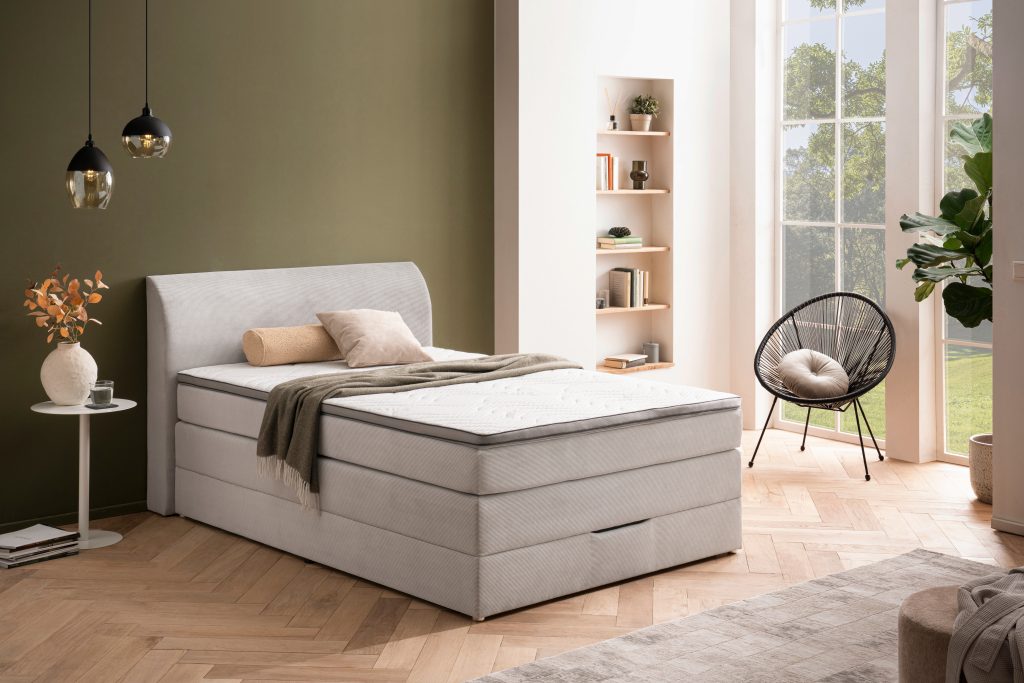 Schlafzimmer mit gepolstertem Boxspringbett, Bank und Bilderwand