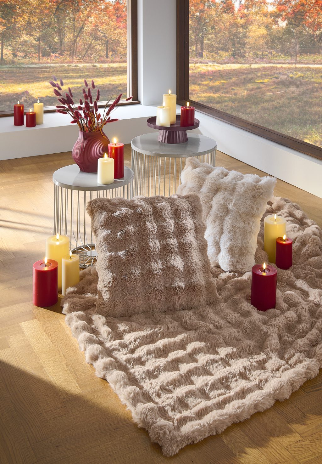 Flauschige Wohndecke und Kissen auf einem Hocker, daneben brennende Kerzen