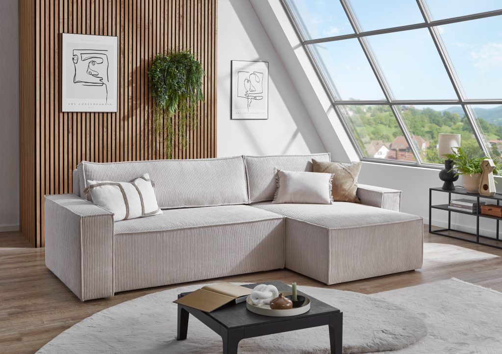 Helles Ecksofa aus Breitcord unter einem Dachfenster, dahinter eine Holzlattenwand