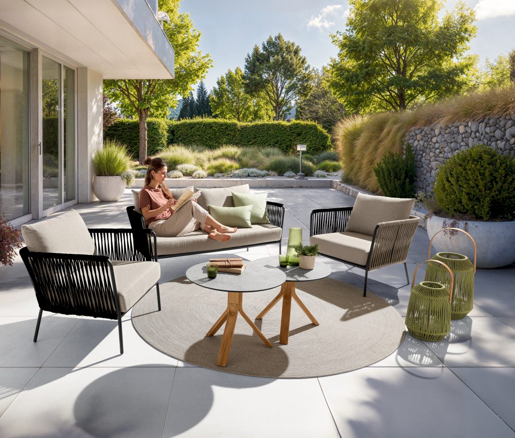 Frau liest auf einer Gartenlounge, Terrasse mit rundem Teppich und Windlichtern